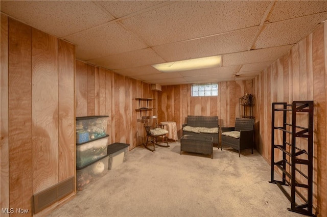 sitting room with visible vents, wooden walls, carpet floors, and a paneled ceiling