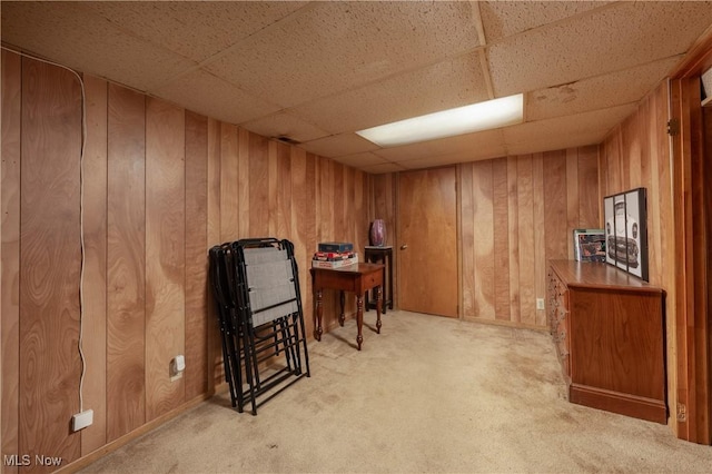 misc room with a drop ceiling, wood walls, and light colored carpet