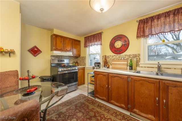 kitchen featuring light countertops, under cabinet range hood, stainless steel gas range oven, a sink, and light tile patterned floors
