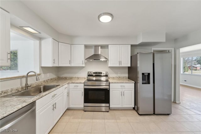 kitchen with a sink, white cabinetry, appliances with stainless steel finishes, wall chimney range hood, and baseboards
