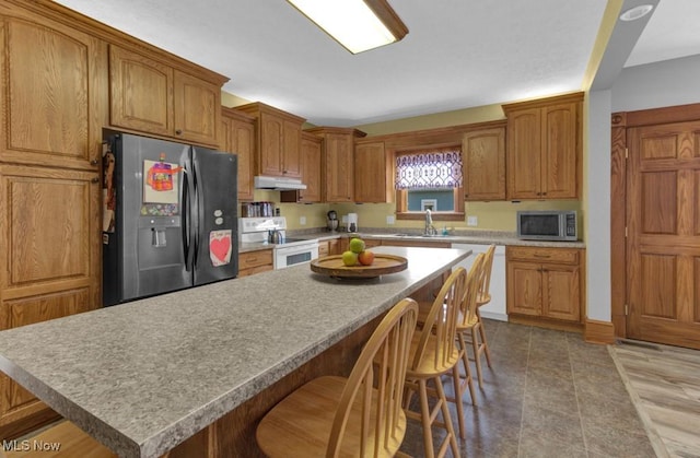 kitchen featuring under cabinet range hood, brown cabinets, a kitchen breakfast bar, and white appliances