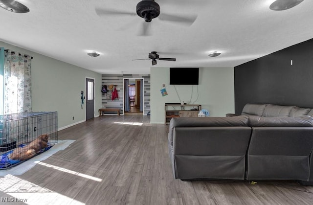 living area with a ceiling fan, a textured ceiling, baseboards, and wood finished floors