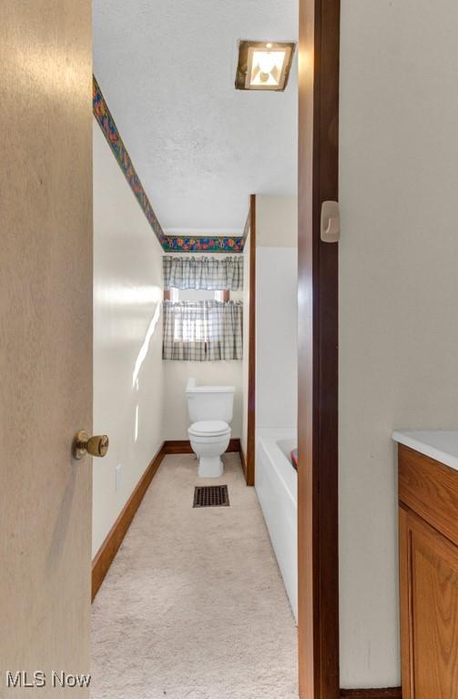 bathroom with a bath, baseboards, toilet, and vanity