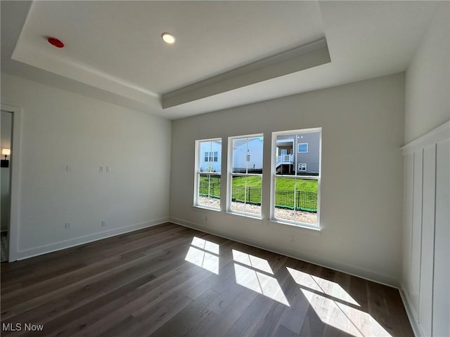 spare room with dark wood-style flooring, baseboards, recessed lighting, and a raised ceiling
