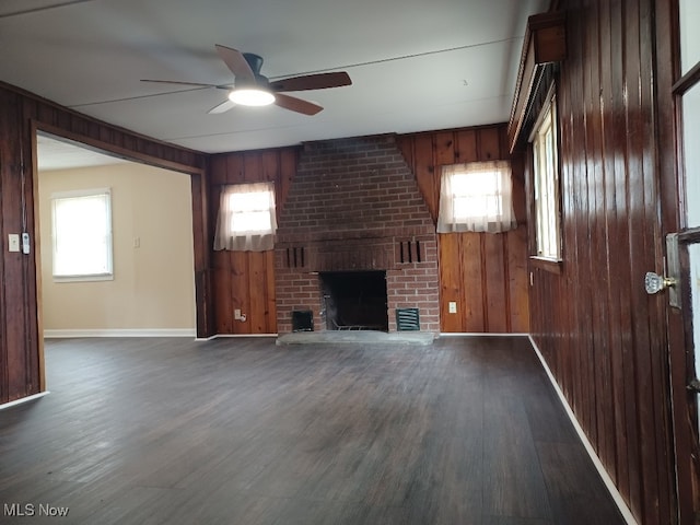 unfurnished living room with dark wood-style floors, ceiling fan, a fireplace, and wooden walls