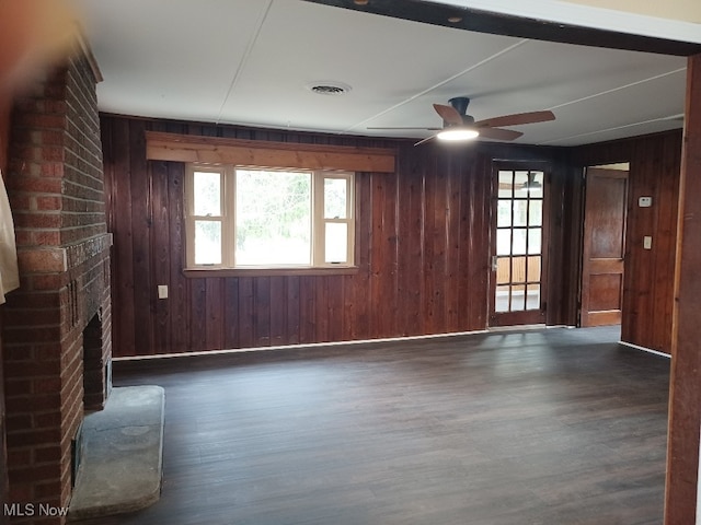 unfurnished living room featuring ceiling fan, a fireplace, visible vents, wood finished floors, and wooden walls