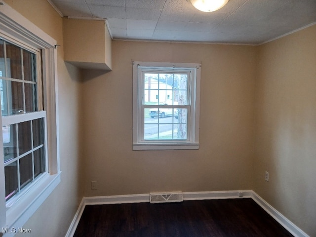 spare room with dark wood-type flooring, visible vents, and baseboards