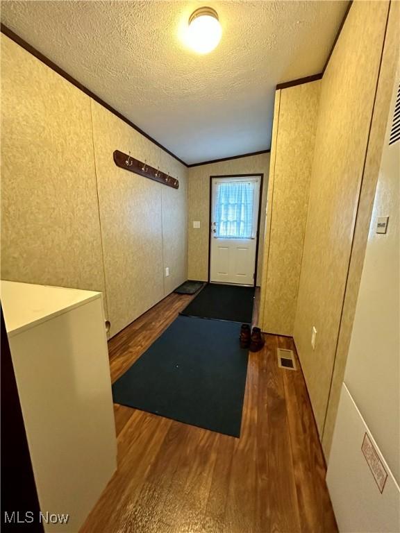interior space featuring wood finished floors, a textured ceiling, lofted ceiling, visible vents, and ornamental molding