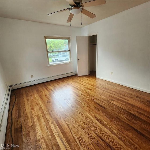 unfurnished bedroom with a baseboard heating unit, baseboards, a baseboard radiator, a closet, and wood finished floors