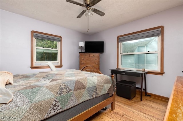 bedroom with baseboards, a textured ceiling, light wood-style flooring, and a ceiling fan
