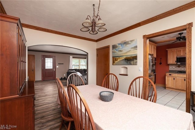 dining space featuring ornamental molding, arched walkways, ceiling fan with notable chandelier, and light wood-type flooring