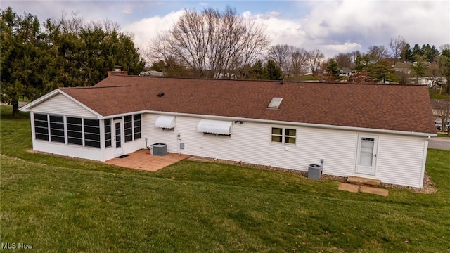 back of property with a sunroom, roof with shingles, central AC unit, a yard, and a chimney