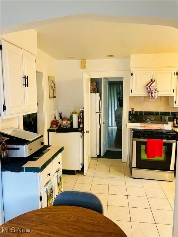1655 Ivydale Rd, Cleveland Heights, OH 44118 - kitchen with decorative backsplash, white cabinetry, gas range, light tile patterned floors, and freestanding refrigerator