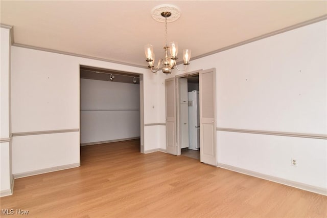 unfurnished dining area featuring ornamental molding, a notable chandelier, baseboards, and light wood-style floors