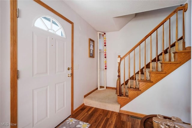 foyer entrance with baseboards, visible vents, wood finished floors, and stairway