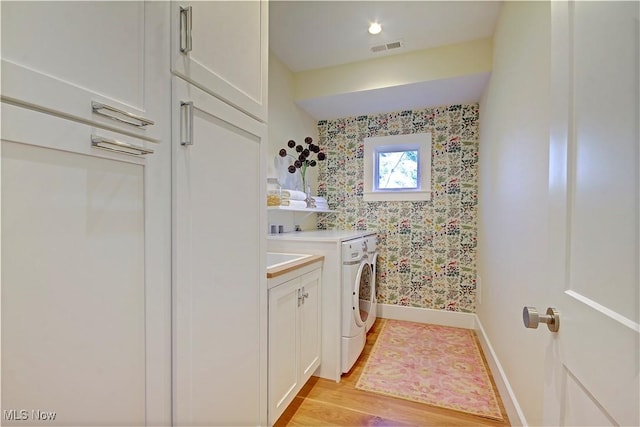 clothes washing area with visible vents, baseboards, light wood-type flooring, cabinet space, and separate washer and dryer