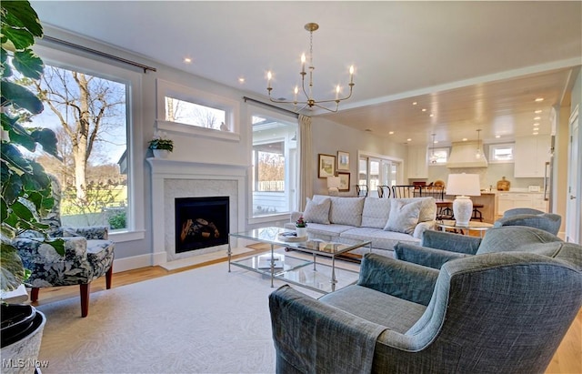 living room featuring a fireplace with flush hearth, a wealth of natural light, a notable chandelier, and light wood-style floors