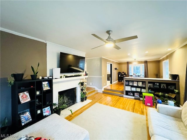 living room featuring baseboards, a fireplace, wood finished floors, ornamental molding, and a ceiling fan