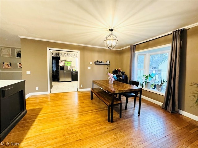 dining room featuring light wood finished floors, baseboards, a notable chandelier, and ornamental molding