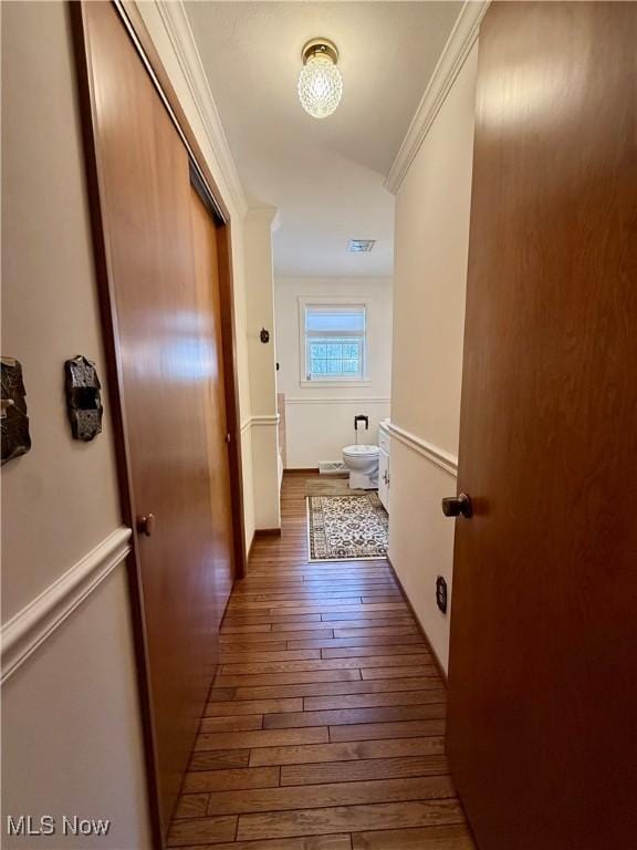 hallway with hardwood / wood-style floors, crown molding, and visible vents