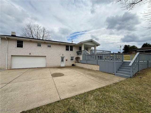 rear view of property featuring brick siding, concrete driveway, a garage, and stairway