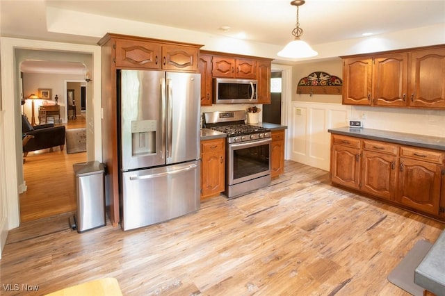 kitchen featuring light wood finished floors, hanging light fixtures, brown cabinetry, stainless steel appliances, and dark countertops