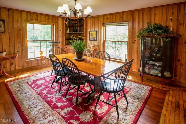 dining area with plenty of natural light, a notable chandelier, wood walls, and wood finished floors