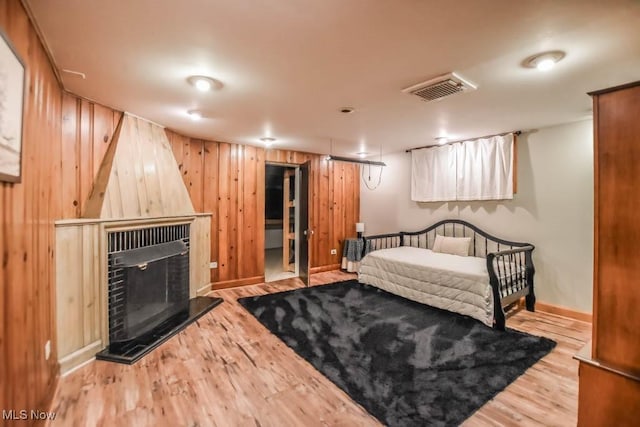bedroom featuring wooden walls, wood finished floors, a fireplace with raised hearth, baseboards, and visible vents