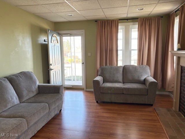 living area featuring a fireplace with flush hearth, baseboards, wood finished floors, and a drop ceiling