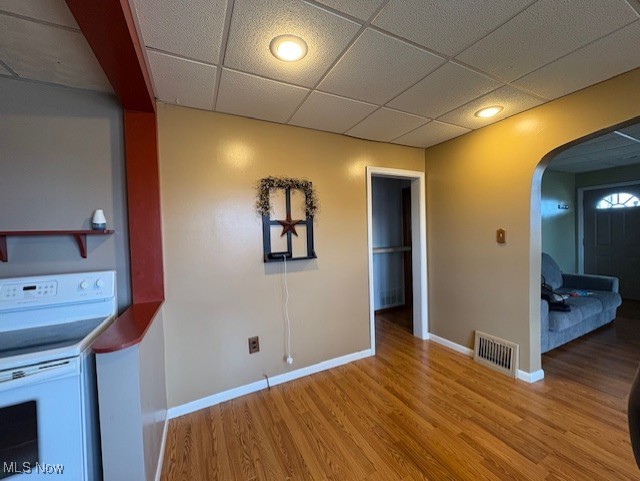 interior space with wood finished floors, baseboards, visible vents, arched walkways, and a drop ceiling