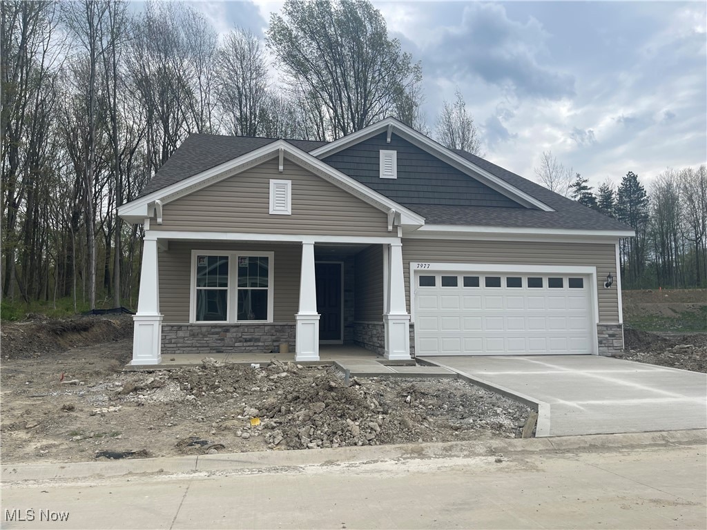 view of front of house with covered porch, an attached garage, stone siding, roof with shingles, and driveway