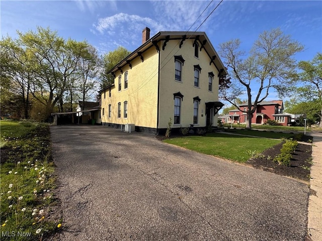 203 W 6th St, Dover, OH 44622 - view of home's exterior featuring a chimney, a carport, aphalt driveway, a yard, and stucco siding