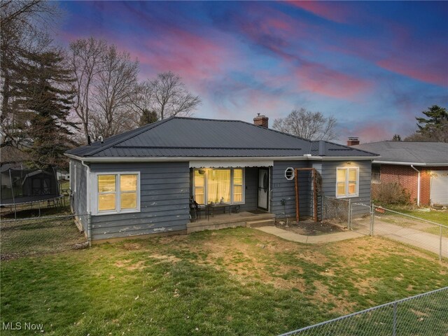 ranch-style house with a trampoline, a chimney, fence, metal roof, and a yard