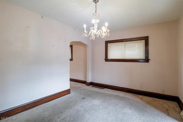 empty room with arched walkways, carpet floors, baseboards, and an inviting chandelier