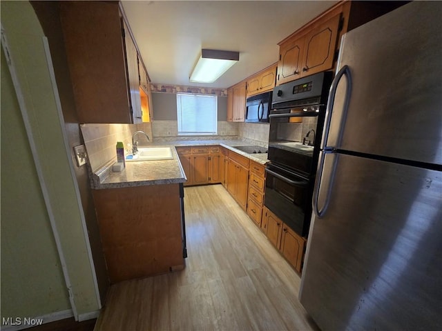 kitchen featuring light wood finished floors, backsplash, black appliances, and a sink