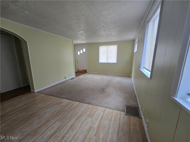 unfurnished room featuring wood finished floors, arched walkways, a textured ceiling, and visible vents