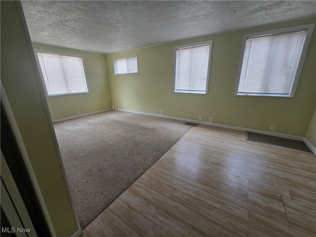 carpeted empty room featuring baseboards, visible vents, wood finished floors, and a textured ceiling