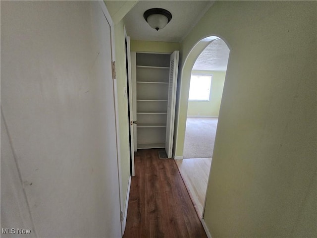 corridor featuring wood finished floors, arched walkways, baseboards, and a textured ceiling