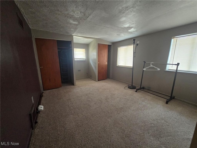 unfurnished bedroom featuring light carpet, multiple windows, and a textured ceiling
