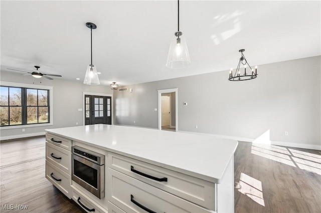 260 Michaels Ct, Cortland, OH 44410 - kitchen featuring open floor plan, stainless steel microwave, white cabinetry, wood finished floors, and hanging light fixtures