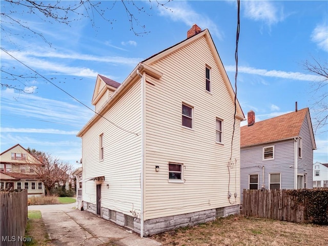 view of side of property with driveway, a chimney, and fence