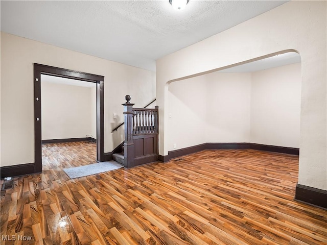 empty room with baseboards, a textured ceiling, and wood finished floors