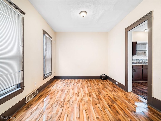 empty room featuring baseboards, visible vents, light wood-type flooring, and a textured ceiling
