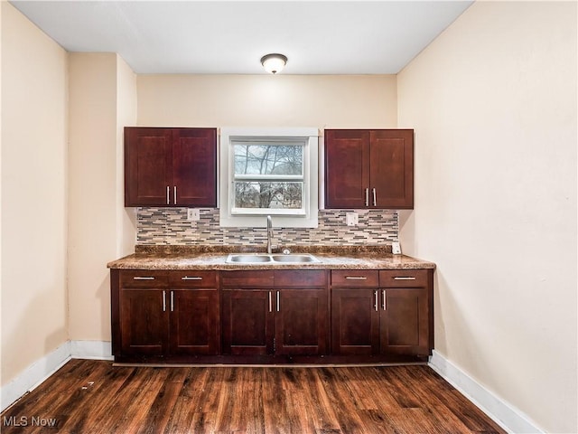 kitchen featuring dark wood finished floors, dark countertops, tasteful backsplash, and a sink