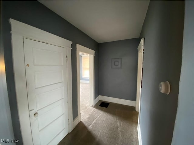 corridor featuring baseboards and dark colored carpet