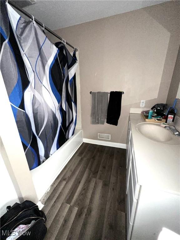 full bathroom featuring shower / bath combo, visible vents, baseboards, wood finished floors, and vanity