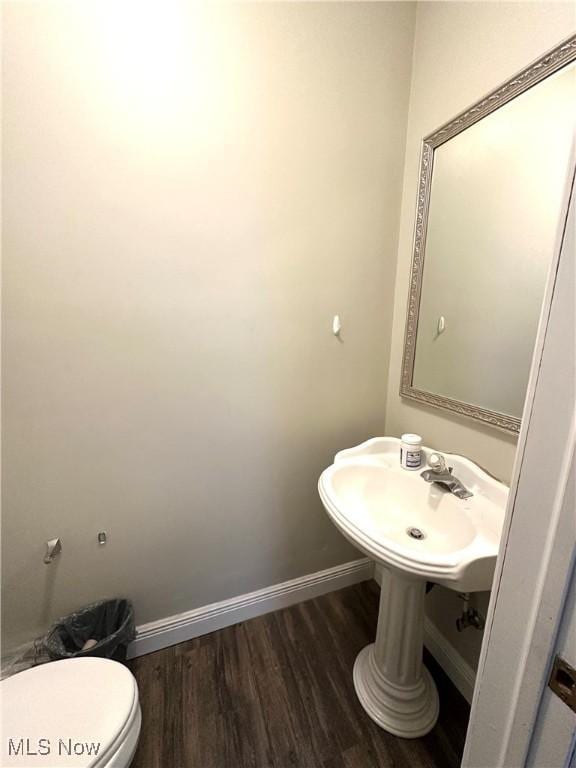 half bath with baseboards, toilet, wood finished floors, and a sink