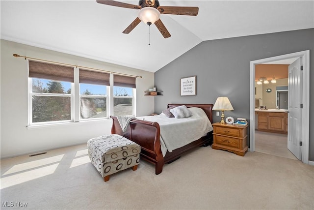 bedroom with vaulted ceiling, light colored carpet, ensuite bathroom, and ceiling fan