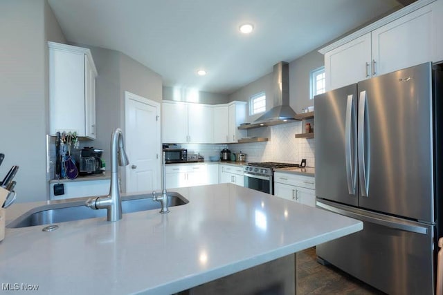 kitchen featuring appliances with stainless steel finishes, wall chimney range hood, a sink, backsplash, and white cabinetry