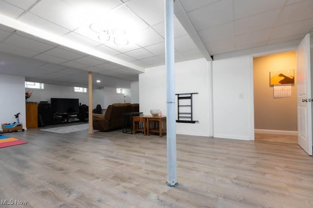 below grade area with wood finished floors, a drop ceiling, and baseboards